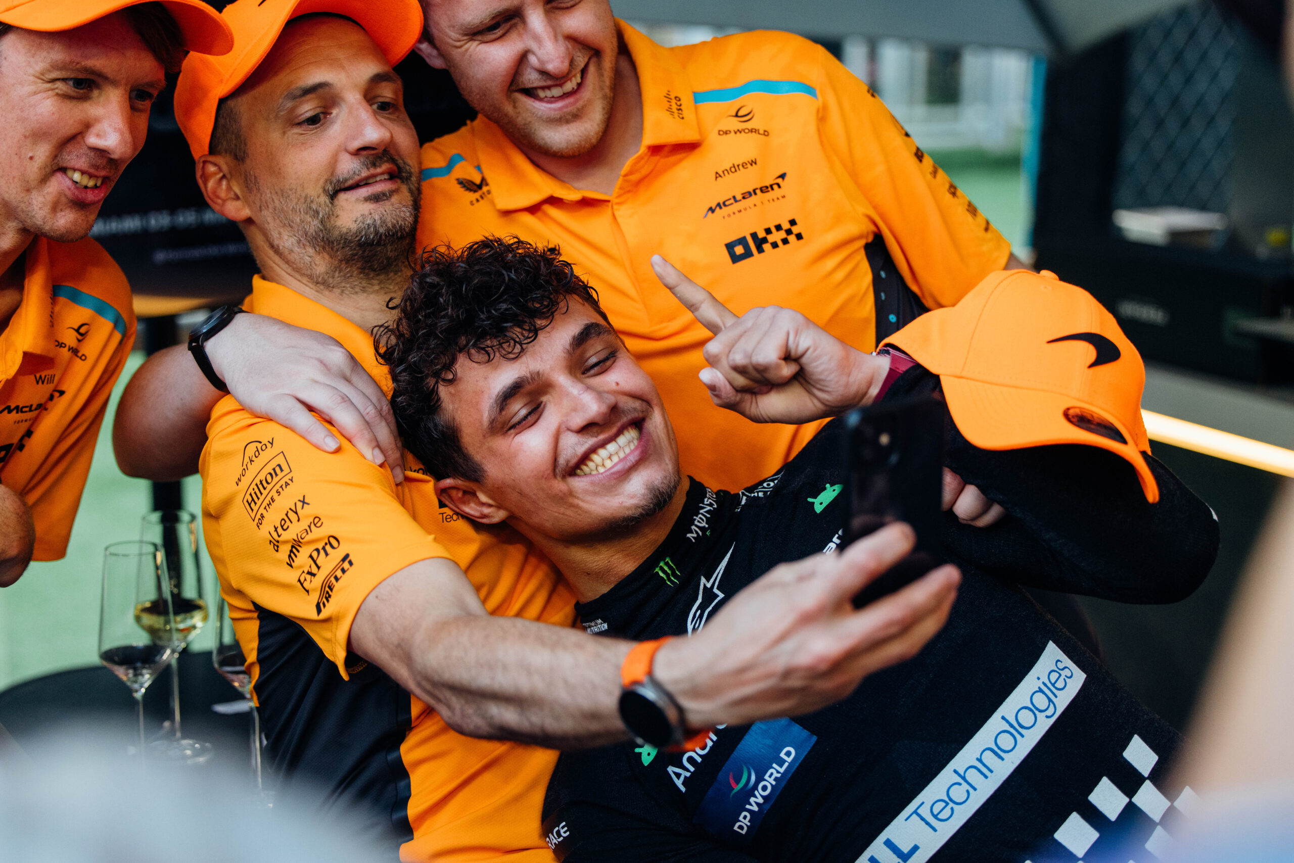 Lando Norris posing with his McLaren crew for a picture. He is celebrating his world championship title by making a number one with his hand for the photo.