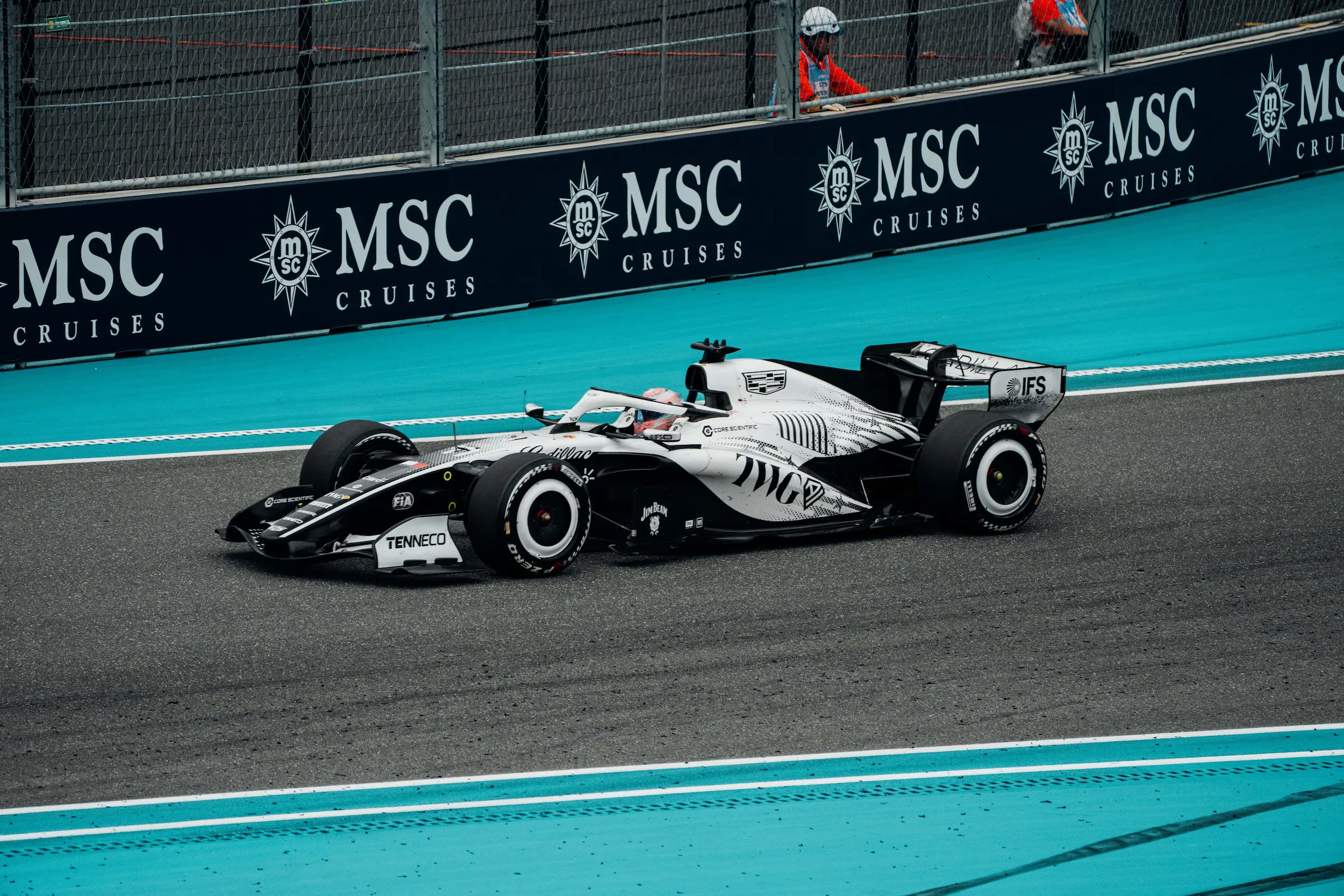 Trackside view of a Cadillac Formula 1 Team car racing along the Miami Grand Prix circuit, with turquoise runoff areas and trackside barriers in the background.