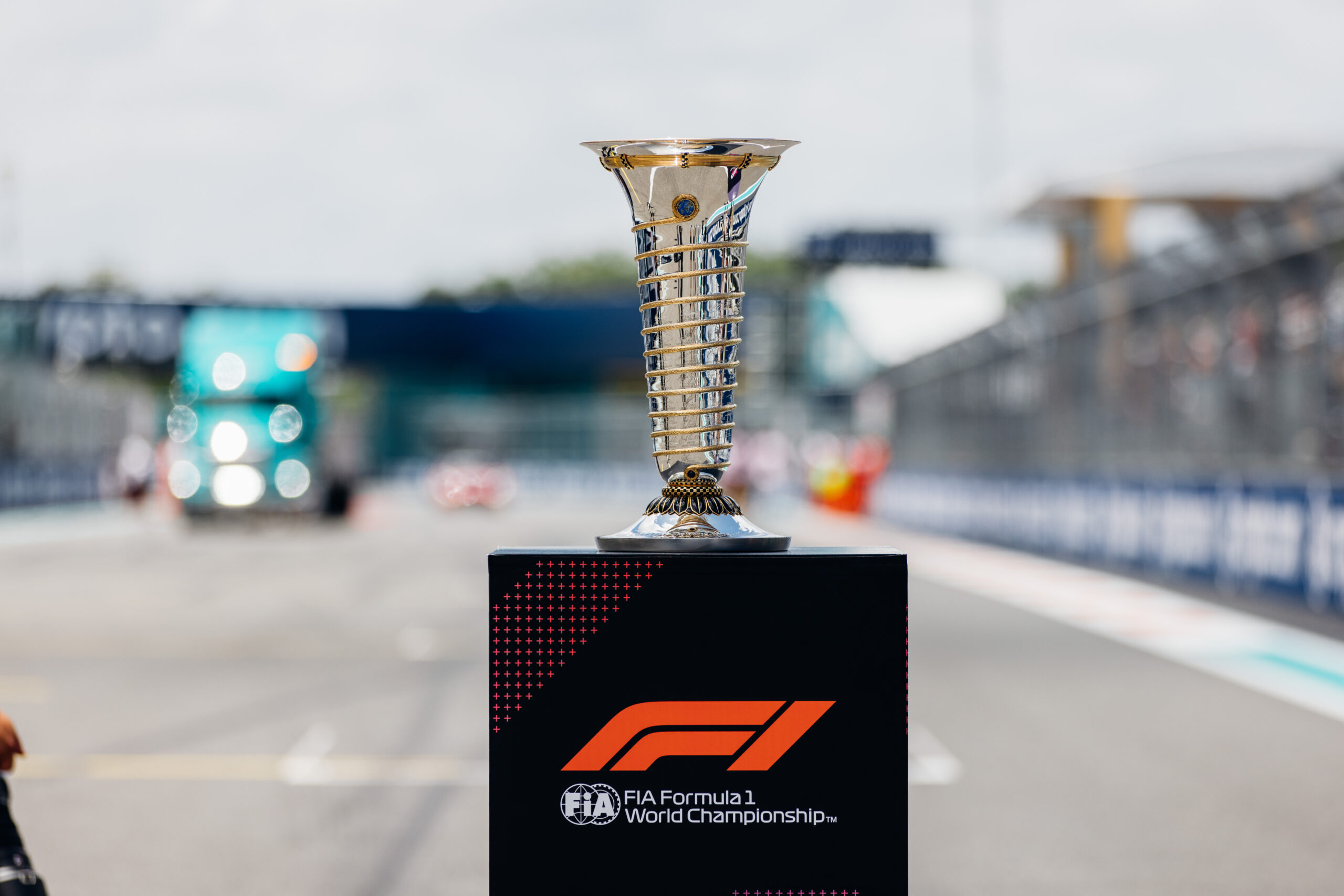 Trophy sits atop F1 podium stand with track in the background.
