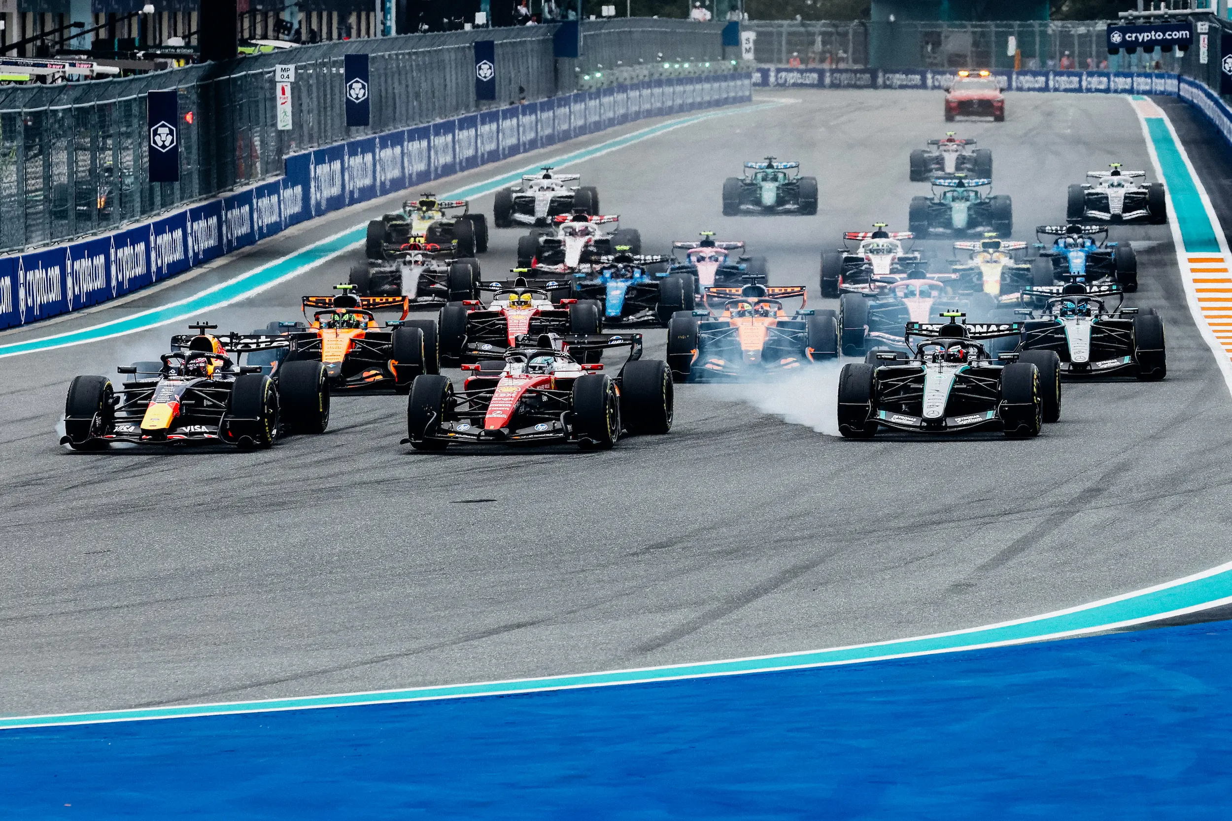 260503_F1MGP_Getty2274316839 Wide-angle view of multiple Formula 1 cars battling for position during the opening laps of the Miami Grand Prix, with tire smoke visible on track.